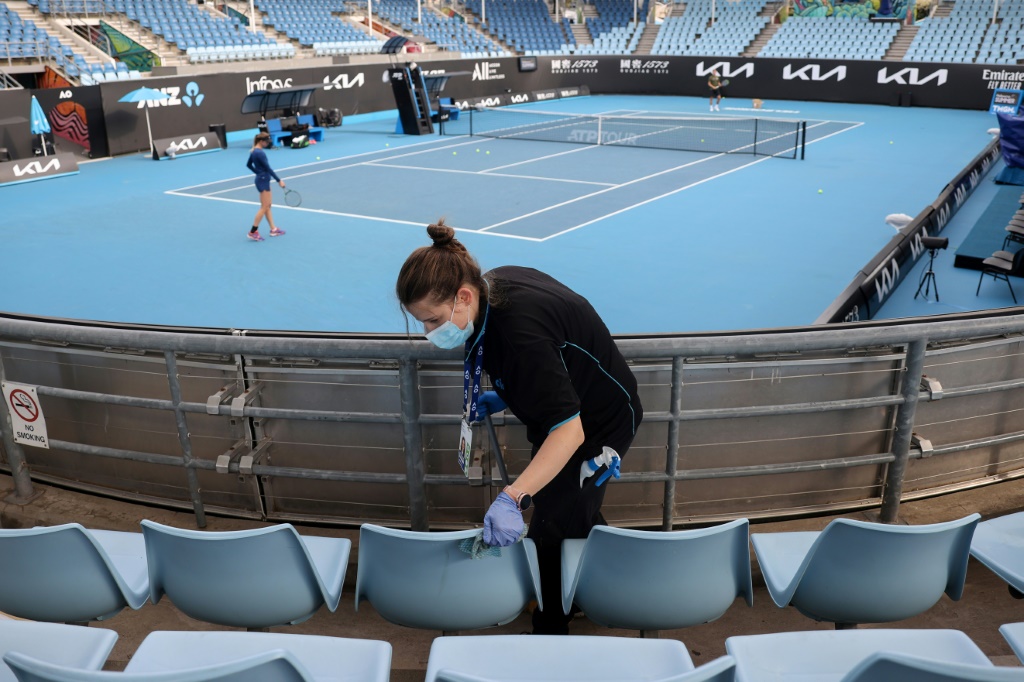 Une personne nettoie les sièges des tribunes pendant que des joueurs s'échauffent sur le court 3 du Melbourne Park