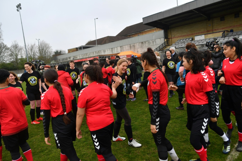 Des députées britanniques saluent l'équipe nationale espoirs afghane, le 29 mars 2022 dans le stade du Dulwich Hamlet FC au sud de Londres, avant leur match organisé par Amnesty International