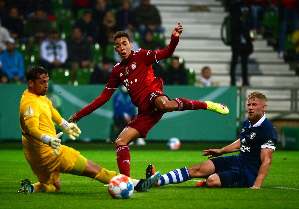 Le milieu de terrain du Bayern Munich Jamal Musiala marque face au gardien de Brême Malte Seemann, lors du 1er tour de la Coupe d'Allemagne, le 25 août 2021 à Brême