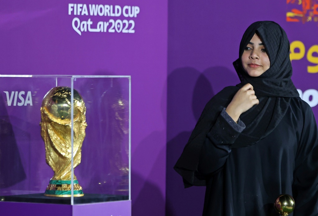 Une jeune femme pose devant le Trophée de la Coupe du monde exposé au Qatar