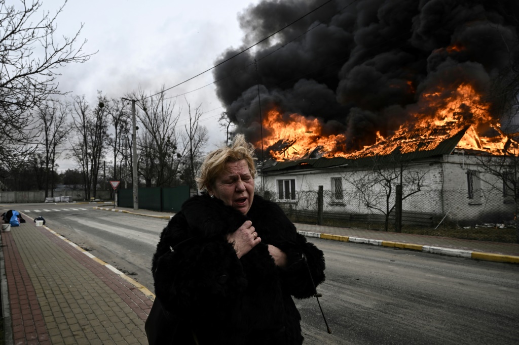 Une femme fuyant devant une maison en flammes le 4 mars 2022 à Irpin dans la banlieu de Kiev