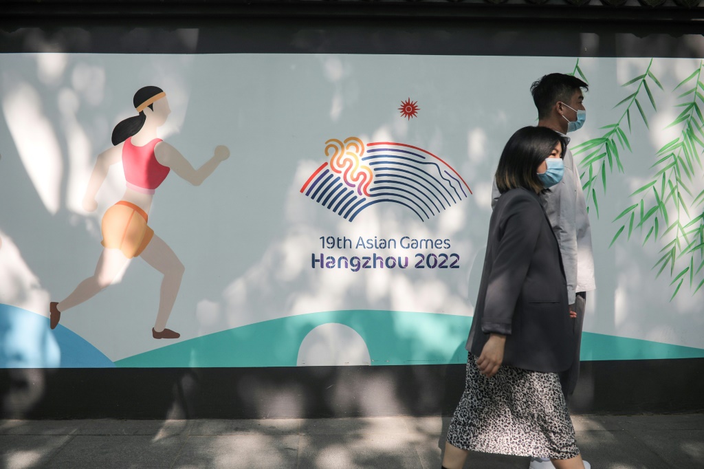 Deux piétons passent devant le logo des Jeux asiatiques, le 8 mai 2022 à Hangzhou, prévus initialement du 10 au 25 septembre, mais reportés pour cause d'épidémie de Covid 19, du 23 septembre au 8 octobre 2023