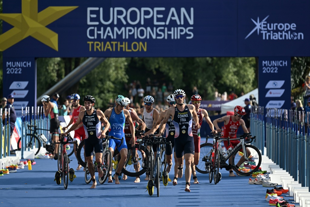 Des athlètes, dont le Français Dorian Coninx, descendent de leur vélo pour débuter l'épreuve de course à pied lors de l'épreuve de triathlon masculin au parc olympique de Munich, le 13 août 2022