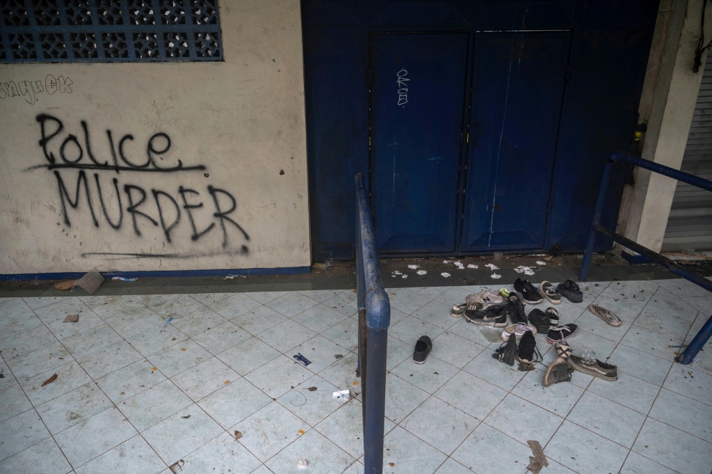 Des chaussures abandonnées au stade Kanjuruhan près d'un graffiti incriminant la police après une bousculade meurtrière lors d'un match de foot, à Malang en Indonésie le 3 octobre 2022