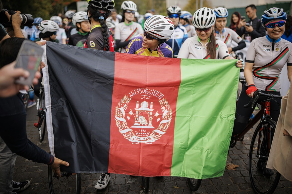 Des concurrentes des championnats d'Afghanistan de cyclisme pour les femmes attendent derrière un drapeau afghan de prendre le départ de la course le 23 octobre 2022 à Aigle (Suisse), la politique des talibans interdisant l'organisation de manifestations sportives pour les femmes en Afghanistan.