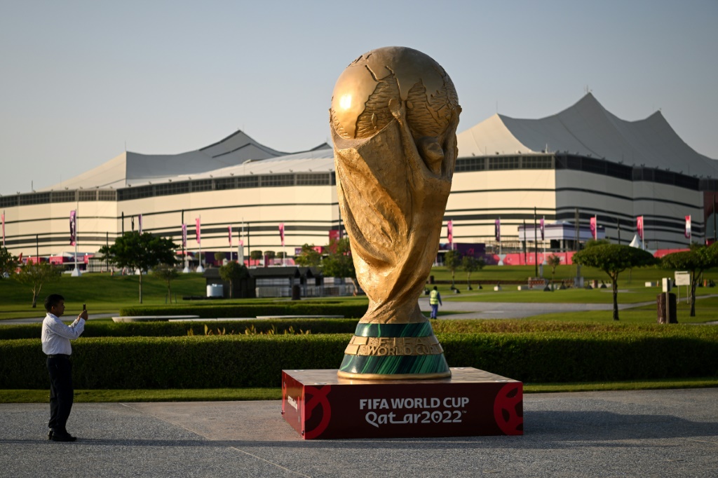 Un homme prend une photo d'une réplique géante du trophée de la Coupe du monde de football de la FIFA devant le stade Al-Bayt de al-Khor (Qatar) le 10 novembre 2022