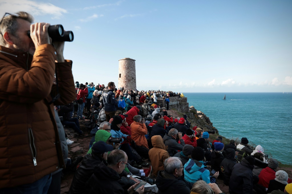 Des spectateurs regardent les voiliers naviguer lors du départ de la Route du Rhum en solitaire, au Cap-Frehel, dans l'ouest de la France, le 9 novembre 2022