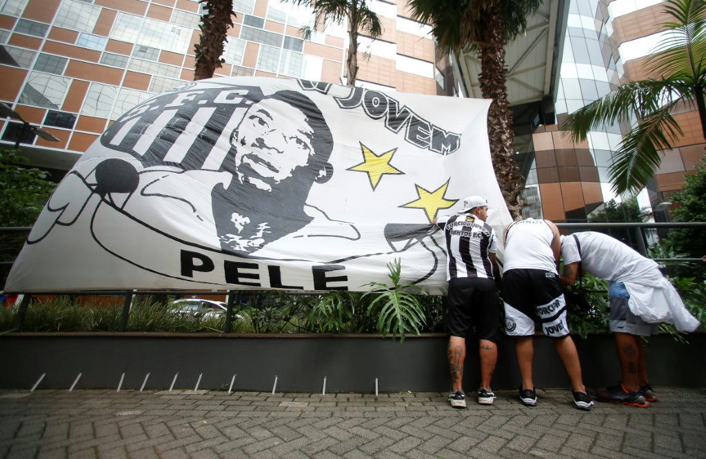 Des fans du club de football Santos installent un drapeau avec le portrait du Brésilien Pelé devant l'hôpital Albert-Einstein où il est soigné pour une infection pulmonaire, le 4 décembre 2022 à Sao Paulo