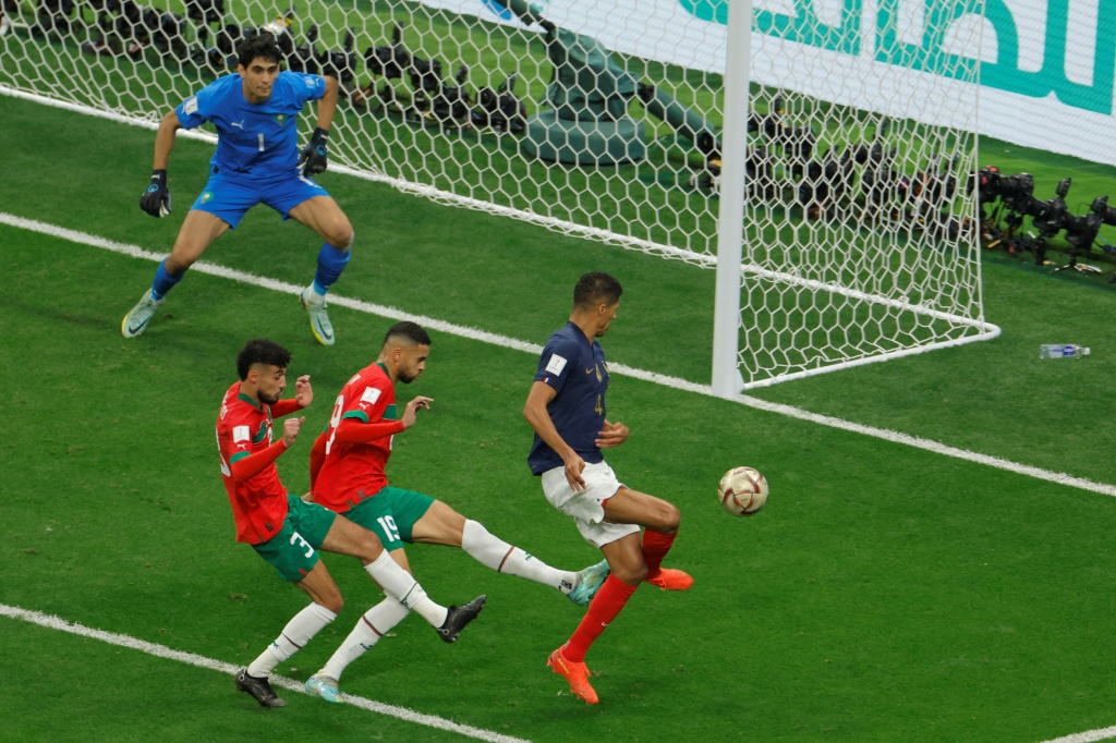 Le défenseur français Raphaël Varane (d) intervient face aux Marocains Youssef En-Nesyri et  Noussair Mazraoui, en demi-finale du Mondial, le 14 décembre à Al Khor