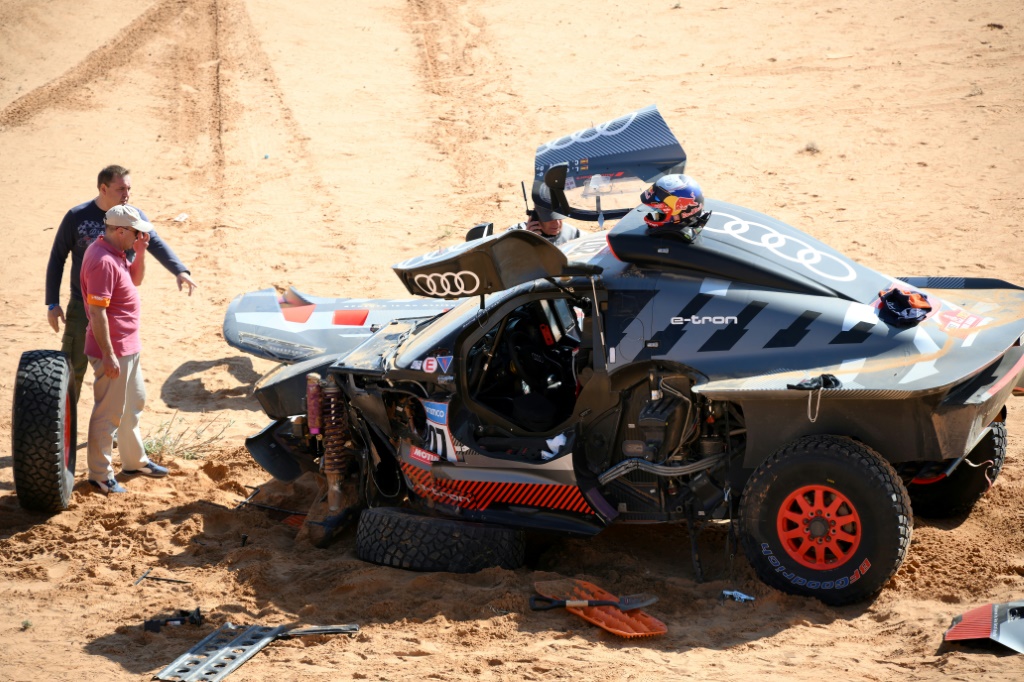 L'Espagnol Carlos Sainz (D) et son copilote Lucas Cruz (C) patientent alors que leur Audi hybride est réparé après un accident lors de la 6e étape du Dakar-2023 entre Haïl et Ryad, en Arabie saoudite, le 6 janvier 2023