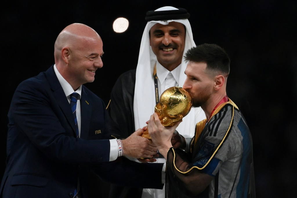 Le président de la Fifa Gianni Infantino (G) remet le trophée de la Coupe du monde à la superstar argentine Lionel Messi (D), sous le regard de l'émir du Qatar, le 18 décembre 2022 à Doha