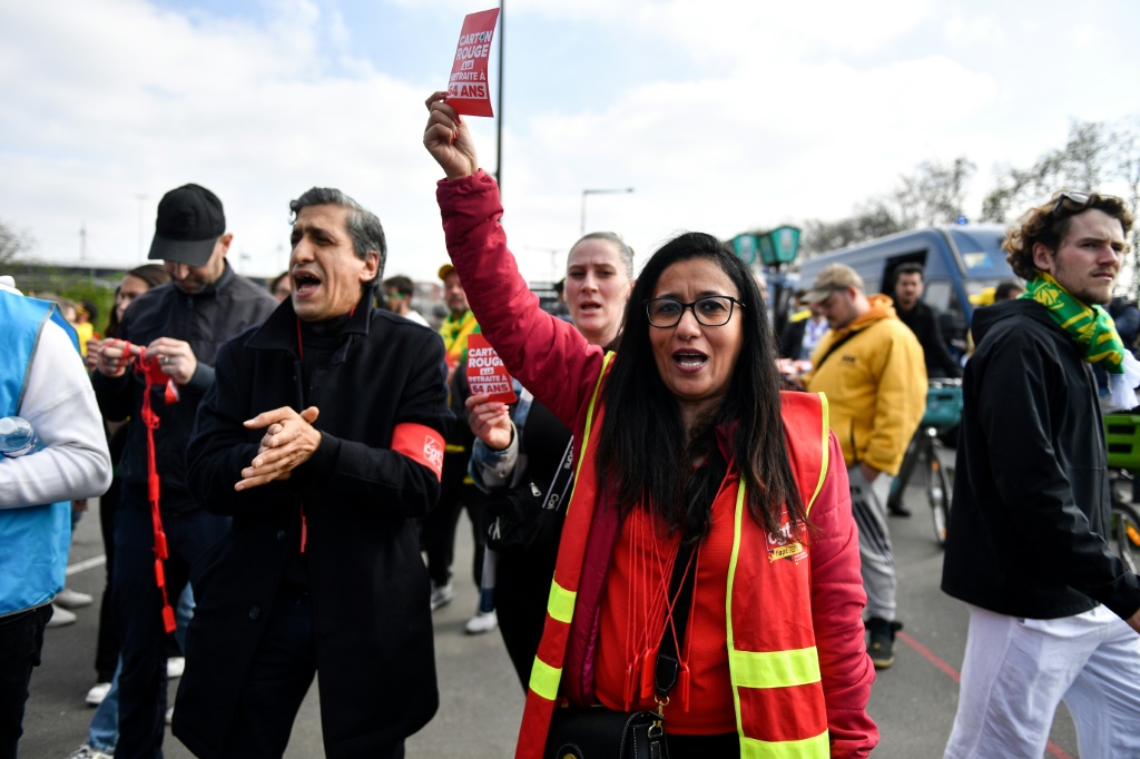 Une militante de la CGT brandit un carton rouge à la retraite à 64 ans à la sortie du métro à Saint-Denis, près de Paris, le 29 avril 2023
